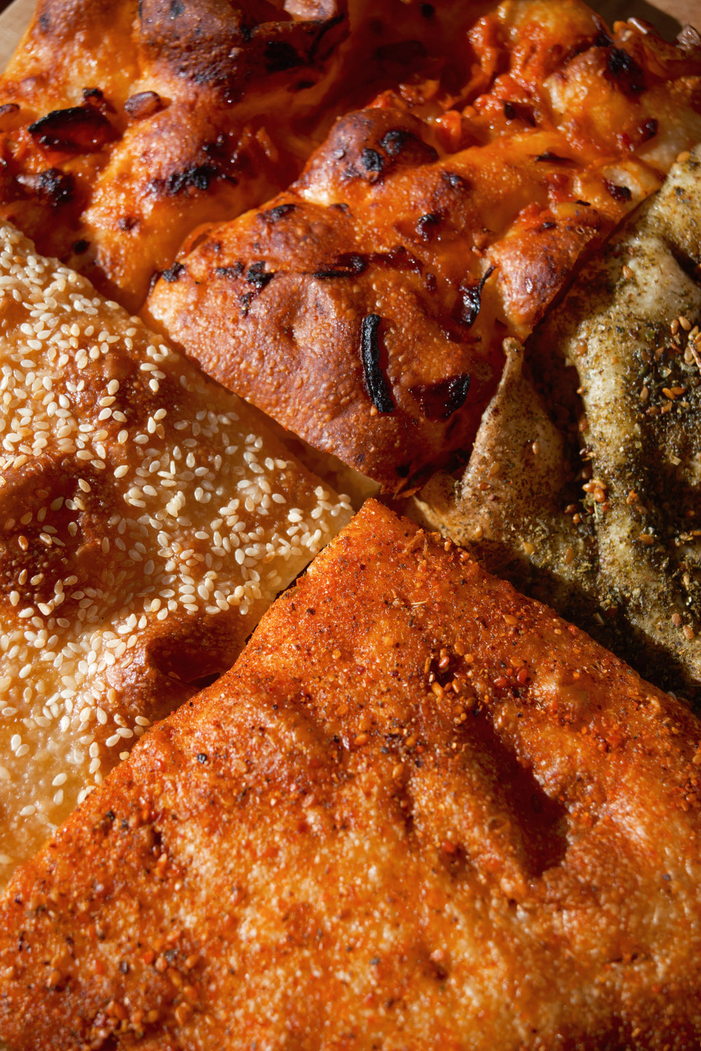 Zeena Bakery focaccia, four different styles (clockwise from top: tomato and onion, zaatar, dukkah, sesame and honey), close up